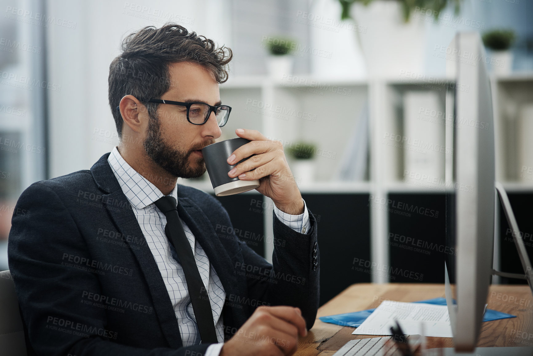 Buy stock photo Shot of a young businessman drinking coffee while working in an office