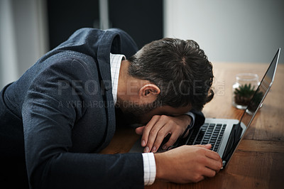 Buy stock photo Shot of a young businessman lying with his head down on a laptop in an office