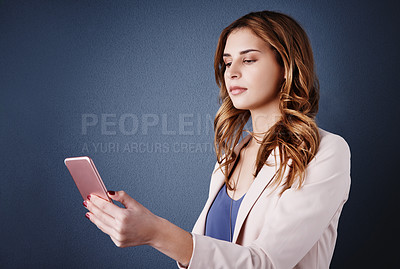 Buy stock photo Studio shot of an attractive young businesswoman using a mobile phone against a dark blue background