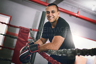 Buy stock photo Portrait of a cheerful young male boxer leaning against ropes inside of a boxing ring at a gym during the day