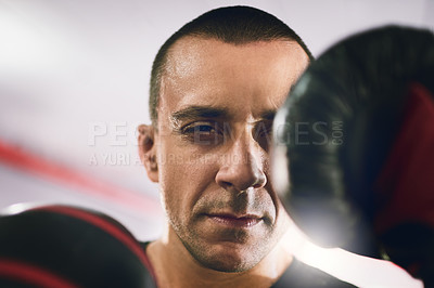 Buy stock photo Portrait of a confident young male boxer wearing boxing gloves while throwing punches at the camera inside of a ring at a gym during the day