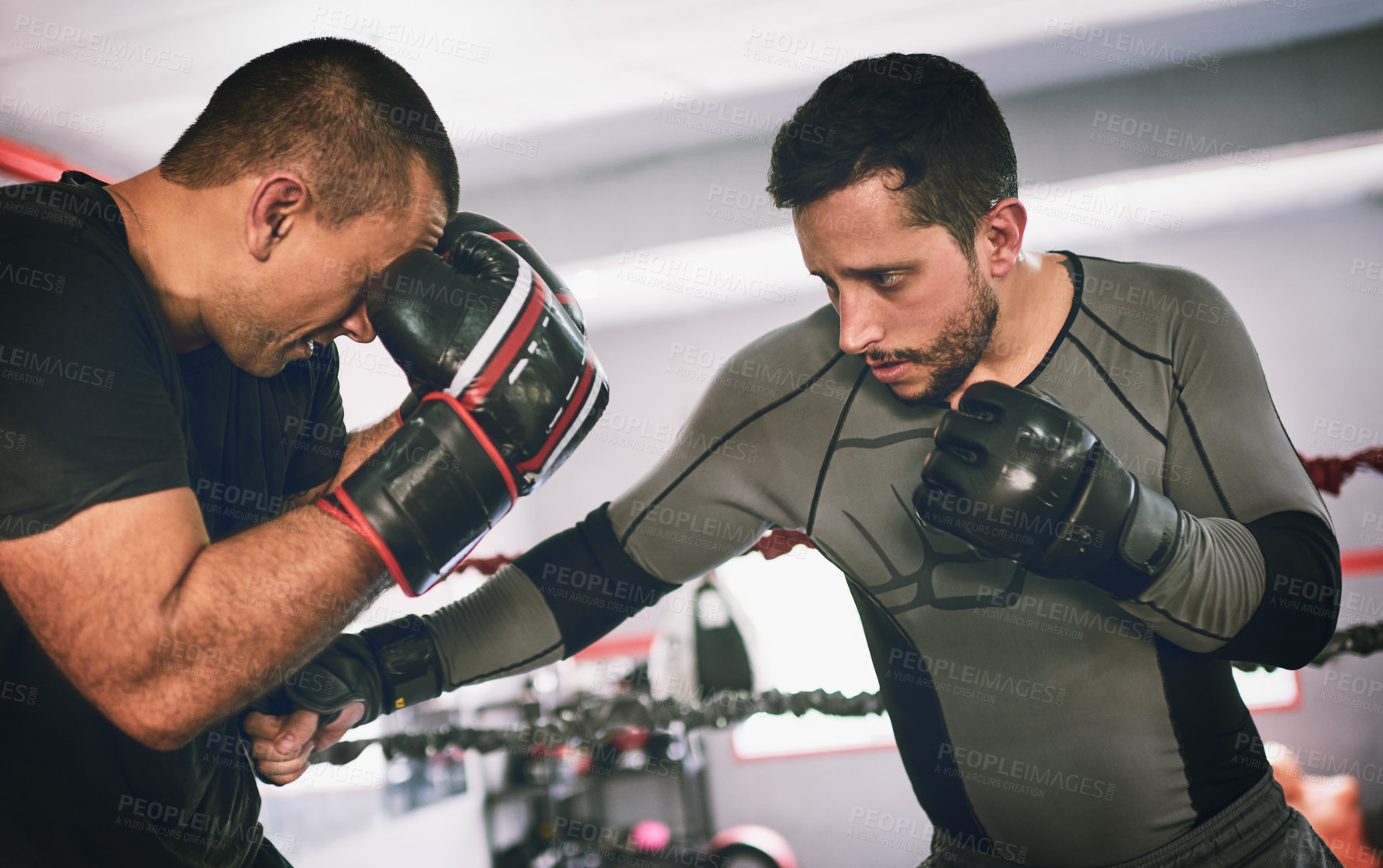 Buy stock photo Shot of two young male boxers facing each other in a training sparing match inside of a boxing ring at a gym during the day