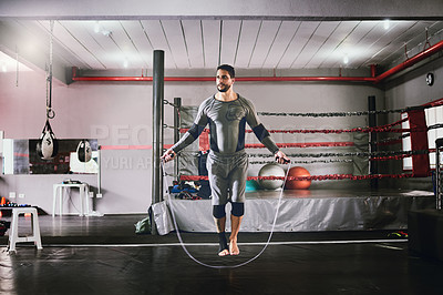 Buy stock photo Shot of a focused young male boxer using a skipping rope for training exercises inside of a gym during the day