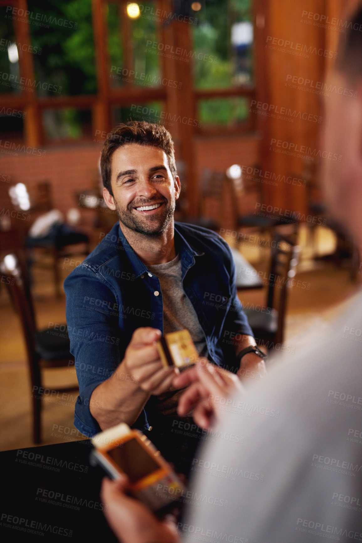 Buy stock photo Shot of a cheerful young man making a payment to a barman through use of a credit card inside a beer brewery during the day