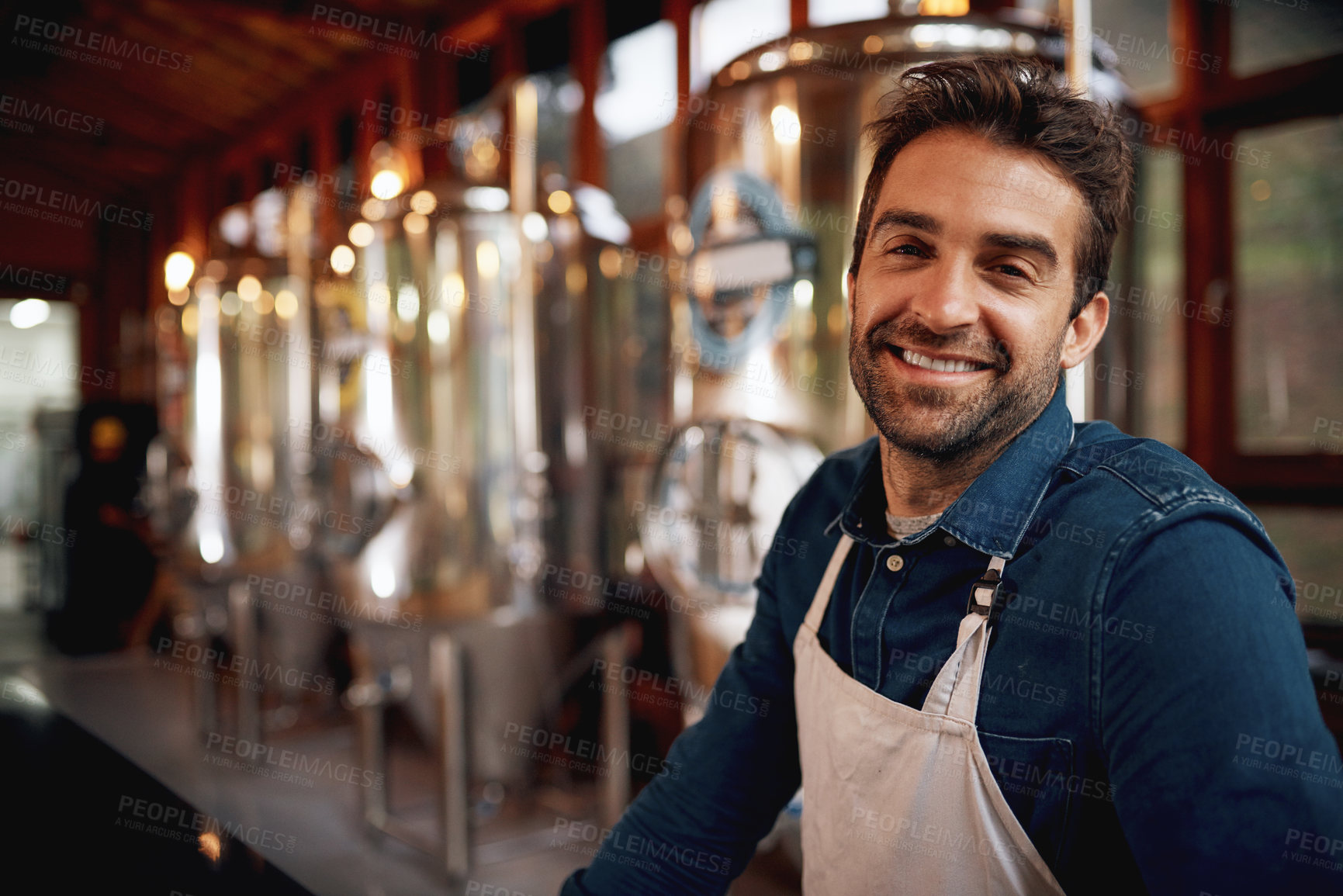 Buy stock photo Portrait of a cheerful young barman leaning on the bar counter waiting for customers to serve inside of a beer brewery