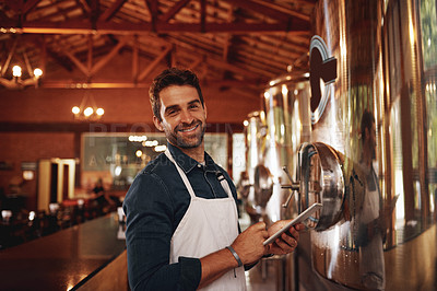 Buy stock photo Portrait of a cheerful young barman browsing on a digital tablet while keeping track of stock inside of a beer brewery during the day