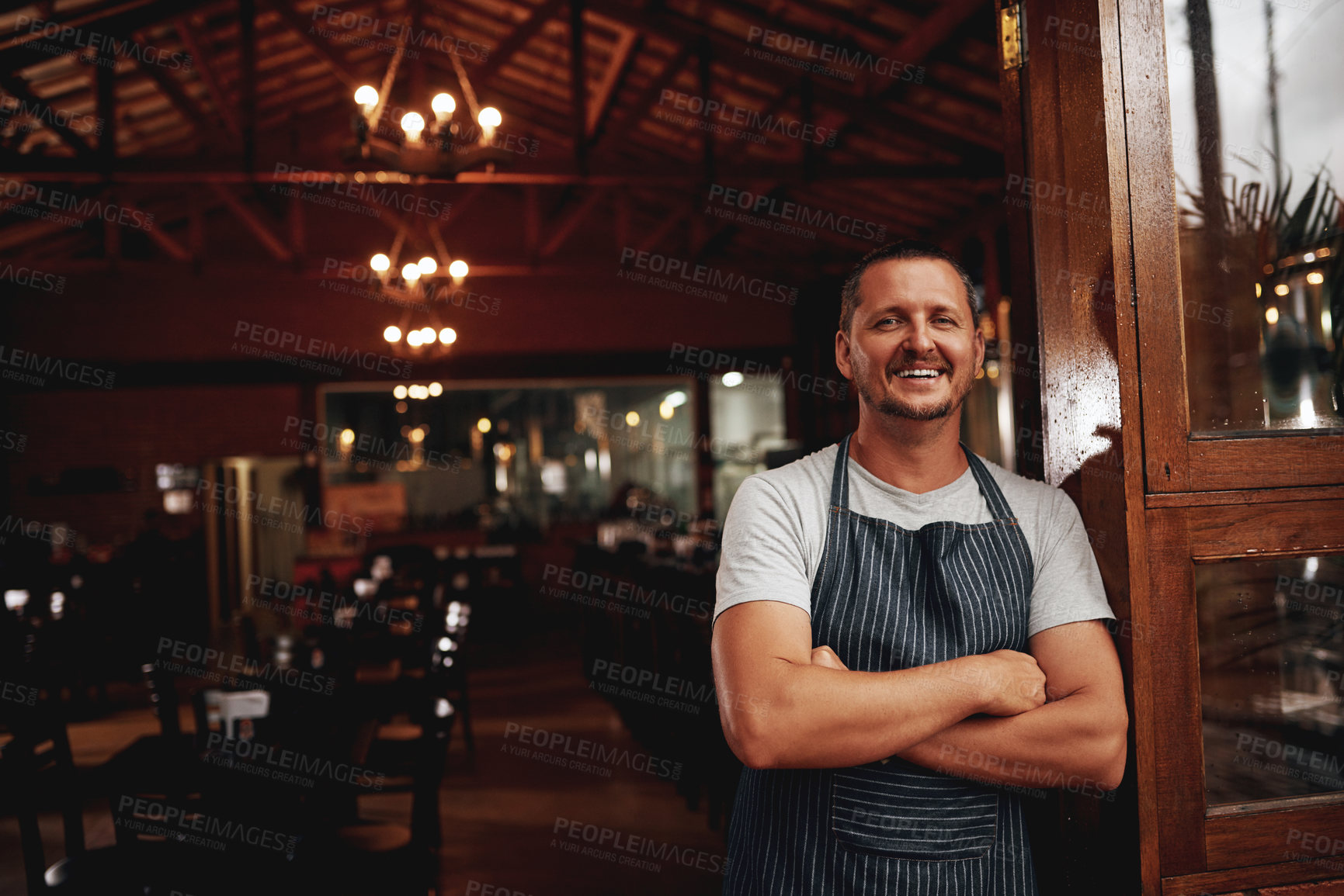 Buy stock photo Portrait of a confident middle aged business owner standing with arms folded under a doorway at a beer brewery during the day