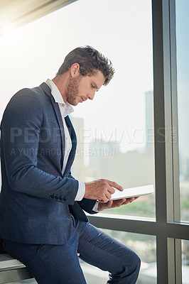 Buy stock photo Shot of a young businessman using a digital tablet in a modern office