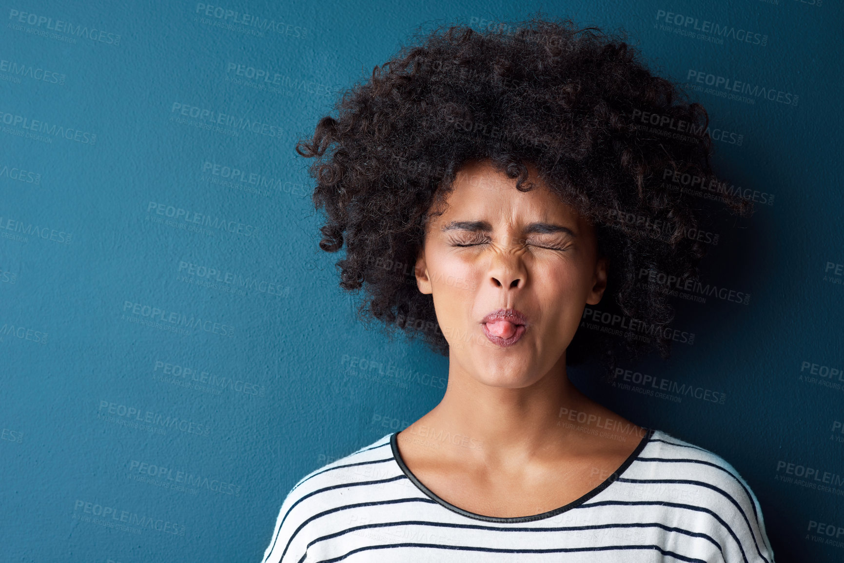 Buy stock photo Portrait, emoji and tongue with facial expression in studio for fun, relax and playful attitude on blue background. Lady, comic and goofy black woman with a funny face, crazy and personality isolated