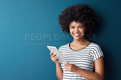 Buy stock photo Studio portrait of an attractive young woman using a digital tablet against a blue background