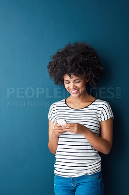 Buy stock photo Studio shot of an attractive young woman using a cellphone against a blue background