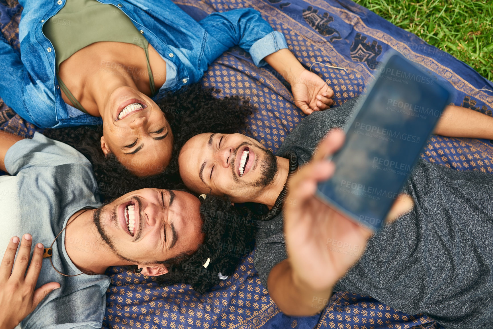 Buy stock photo High angle shot of a group of friends taking a selfie while lying down in a public park