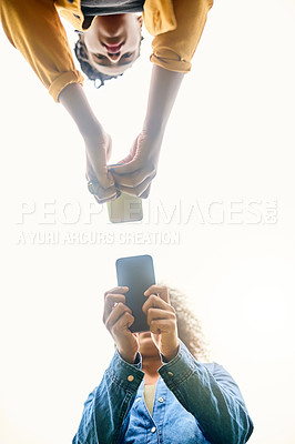 Buy stock photo Low angle shot of beautiful women using cellphones in a public park