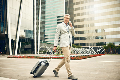 Buy stock photo Shot of a mature businessman talking on a cellphone while walking with a suitcase in the city