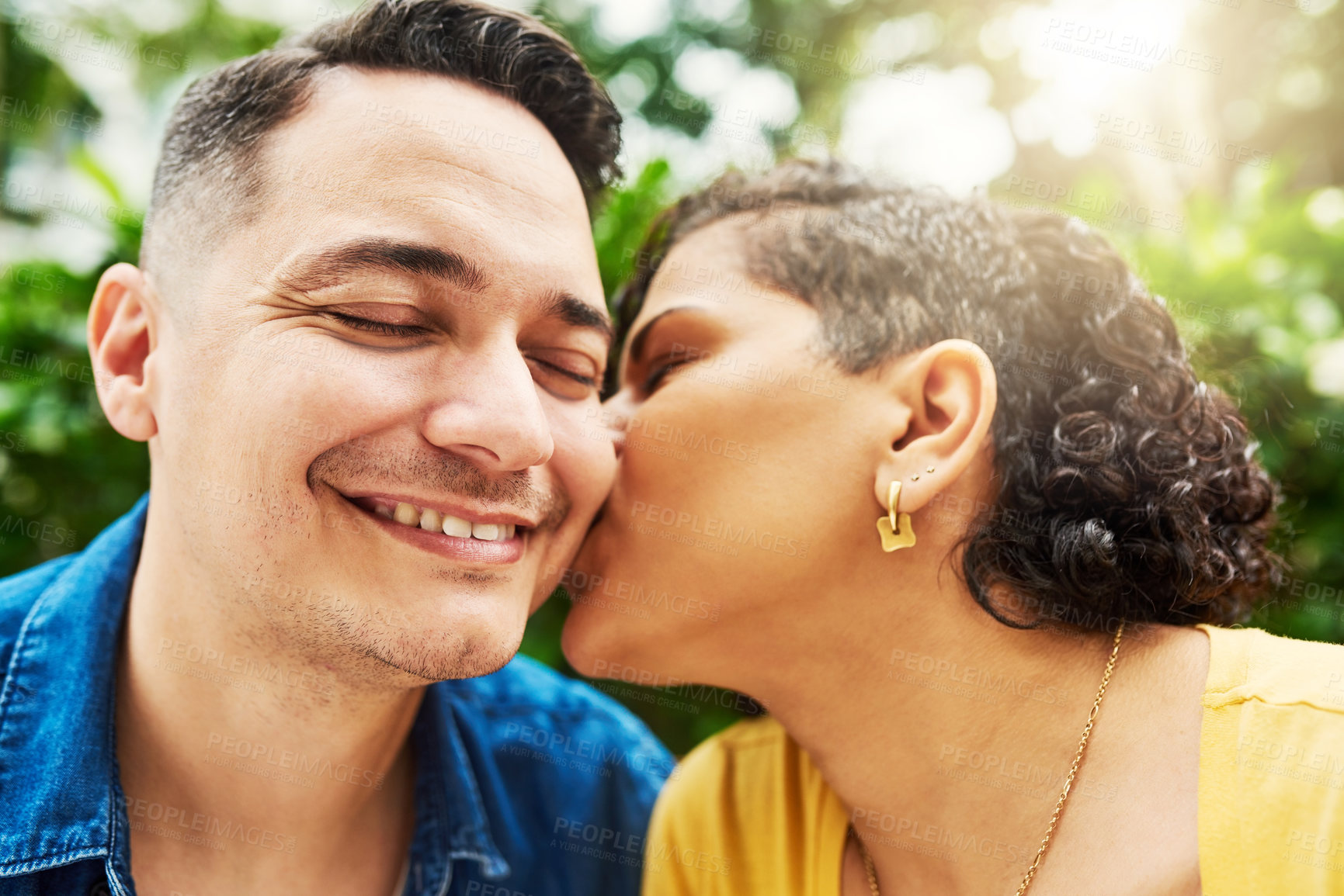 Buy stock photo Cropped shot of a young woman kissing her husband on the cheek while in the park