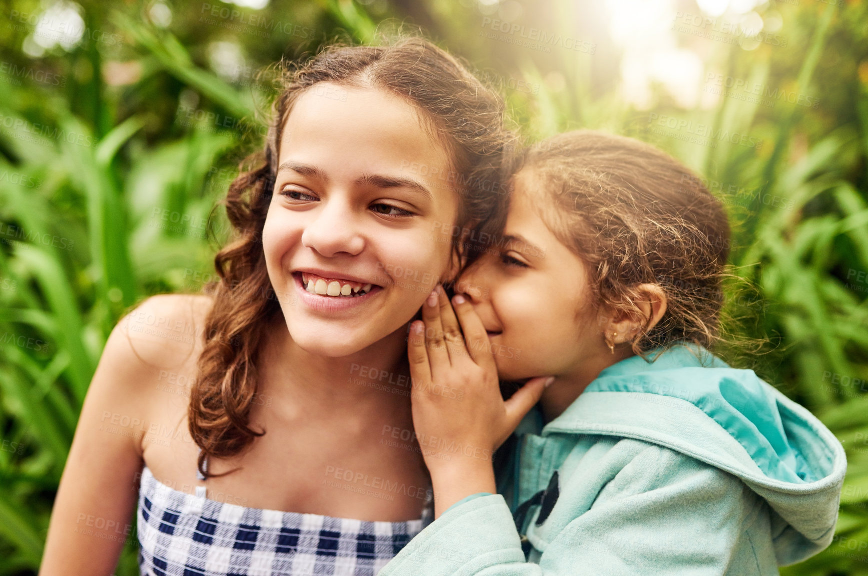 Buy stock photo Cropped shot of an adorable little girl whispering into her sister's ear while out in the park