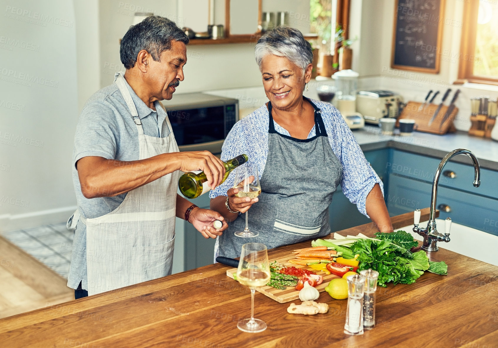 Buy stock photo Shot of a happy mature couple drinking wine while cooking a meal together at home