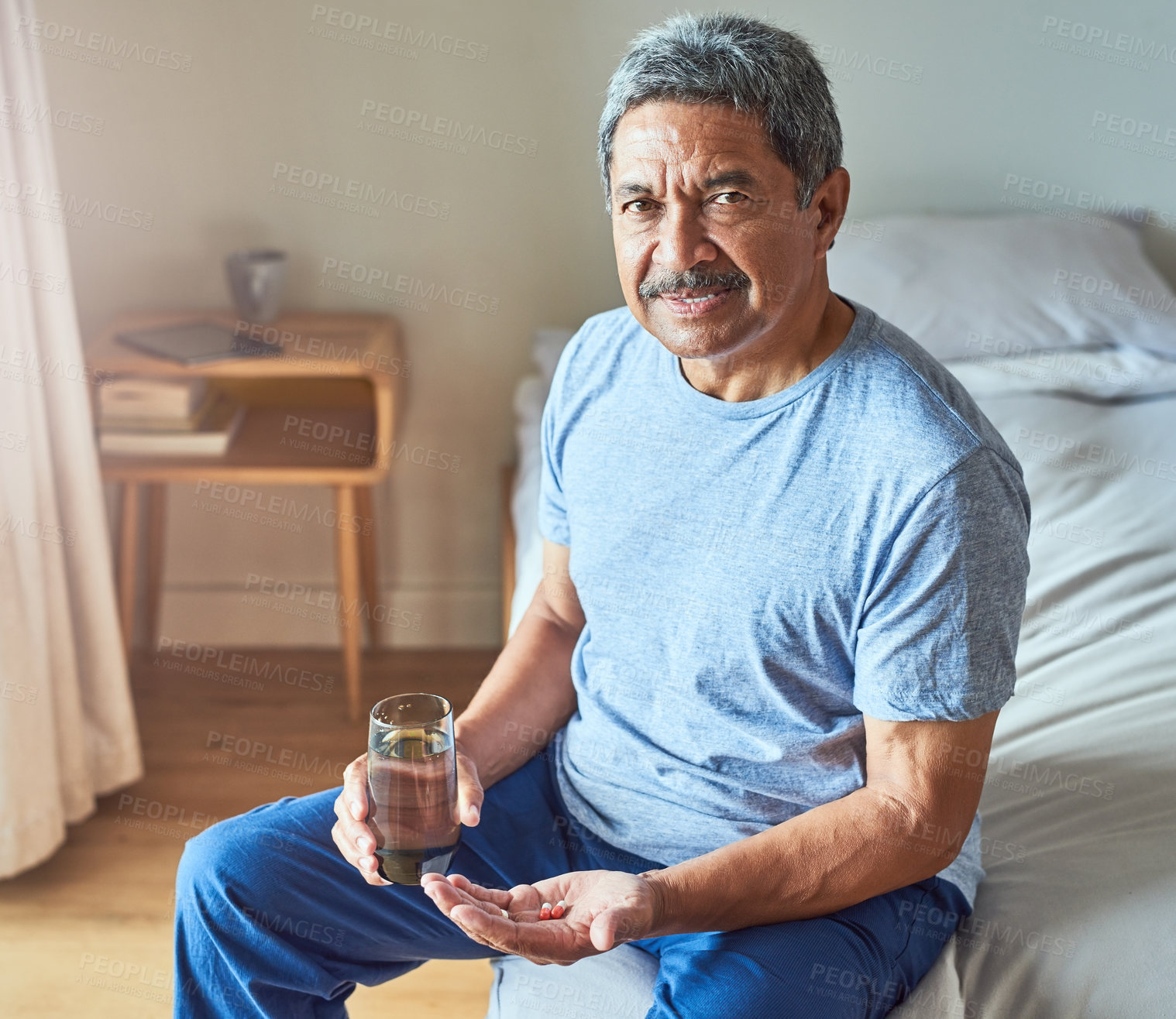 Buy stock photo Portrait of a cheerful mature man seated on his bed and about to drink medication with water in the bedroom at home during the day