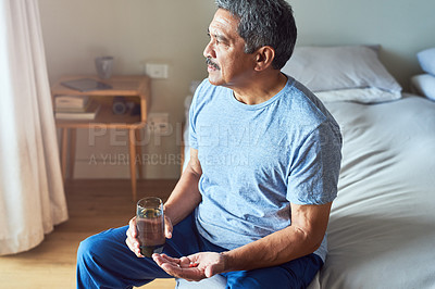 Buy stock photo Shot of a cheerful mature man seated on his bed and about to drink medication with water in the bedroom at home during the day