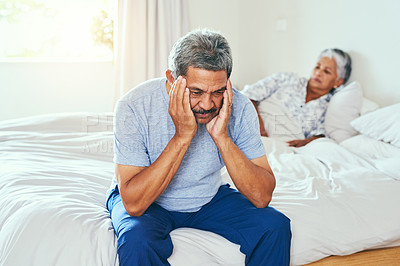 Buy stock photo Shot of a irritated mature man seated on a bed with his wife lying in the background after they had a argument at home