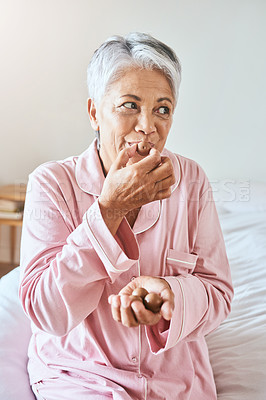 Buy stock photo Shot of a cheerful mature woman enjoying a piece of chocolate while being seated on a bed at home in the morning