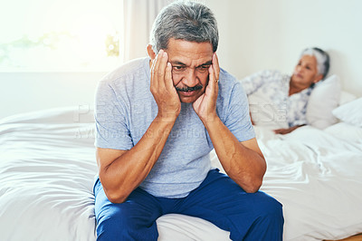 Buy stock photo Shot of a irritated mature man seated on a bed with his wife lying in the background after they had a argument at home