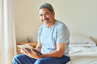 Buy stock photo Portrait of a cheerful mature man browsing on a digital tablet while being seated on his bed at home during the day