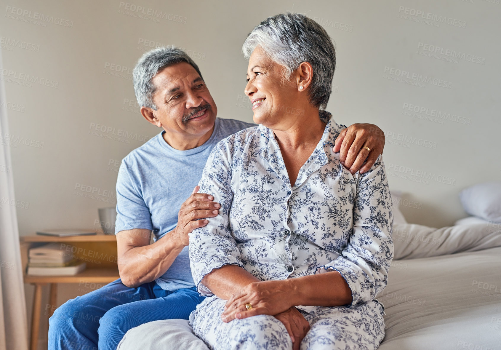 Buy stock photo Portrait of a cheerful mature couple holding each other while being seated on a bed at home during the day