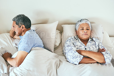 Buy stock photo Shot of an irritated looking mature couple lying in bed facing away from each other after having an argument at home during the day