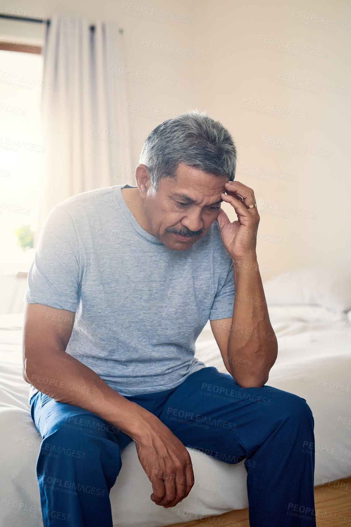 Buy stock photo Shot of a stressed out mature man holding his head in discomfort while being seated on his bed at home