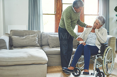 Buy stock photo Shot of a worried looking elderly woman seated in a wheelchair while being supported and held by her husband inside at home during the day