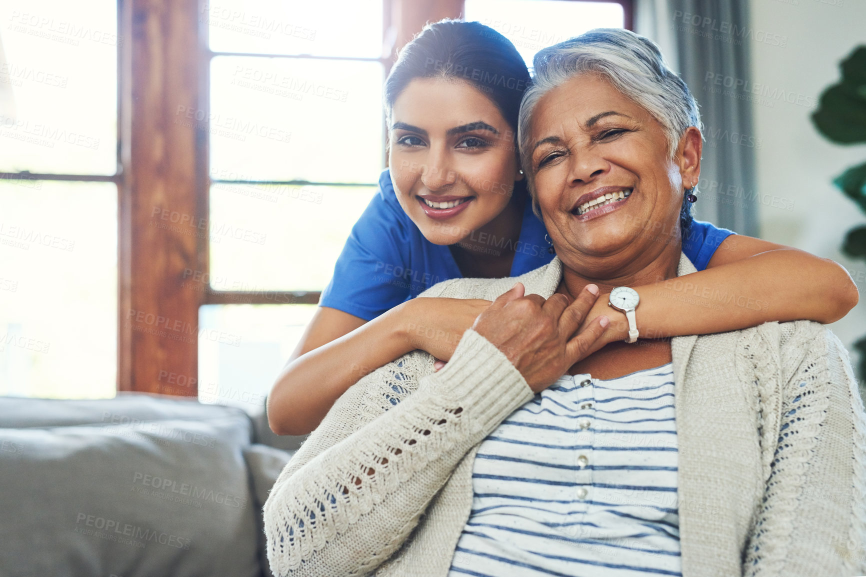 Buy stock photo Portrait of a cheerful young female nurse holding a elderly patient in a wheelchair as support inside at home during the day