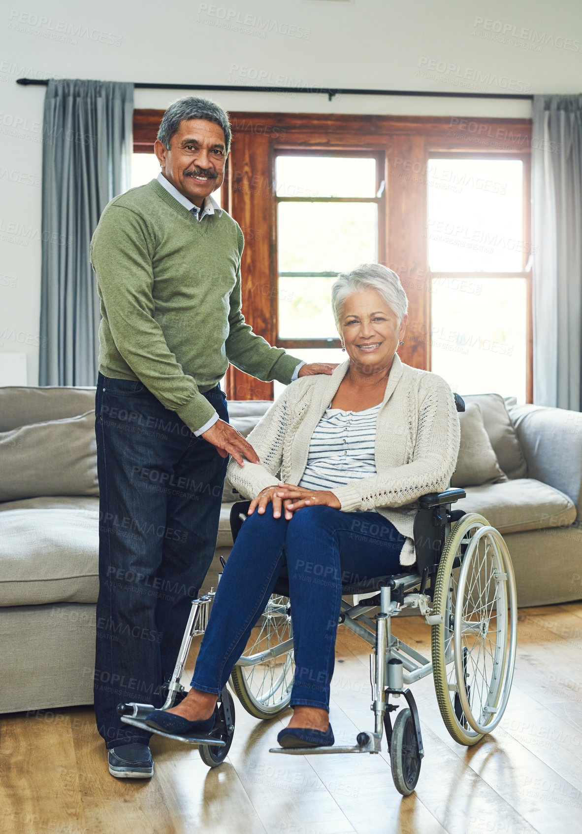 Buy stock photo Portrait of a cheerful elderly woman seated in a wheelchair while being supported and held by her husband inside at home during the day