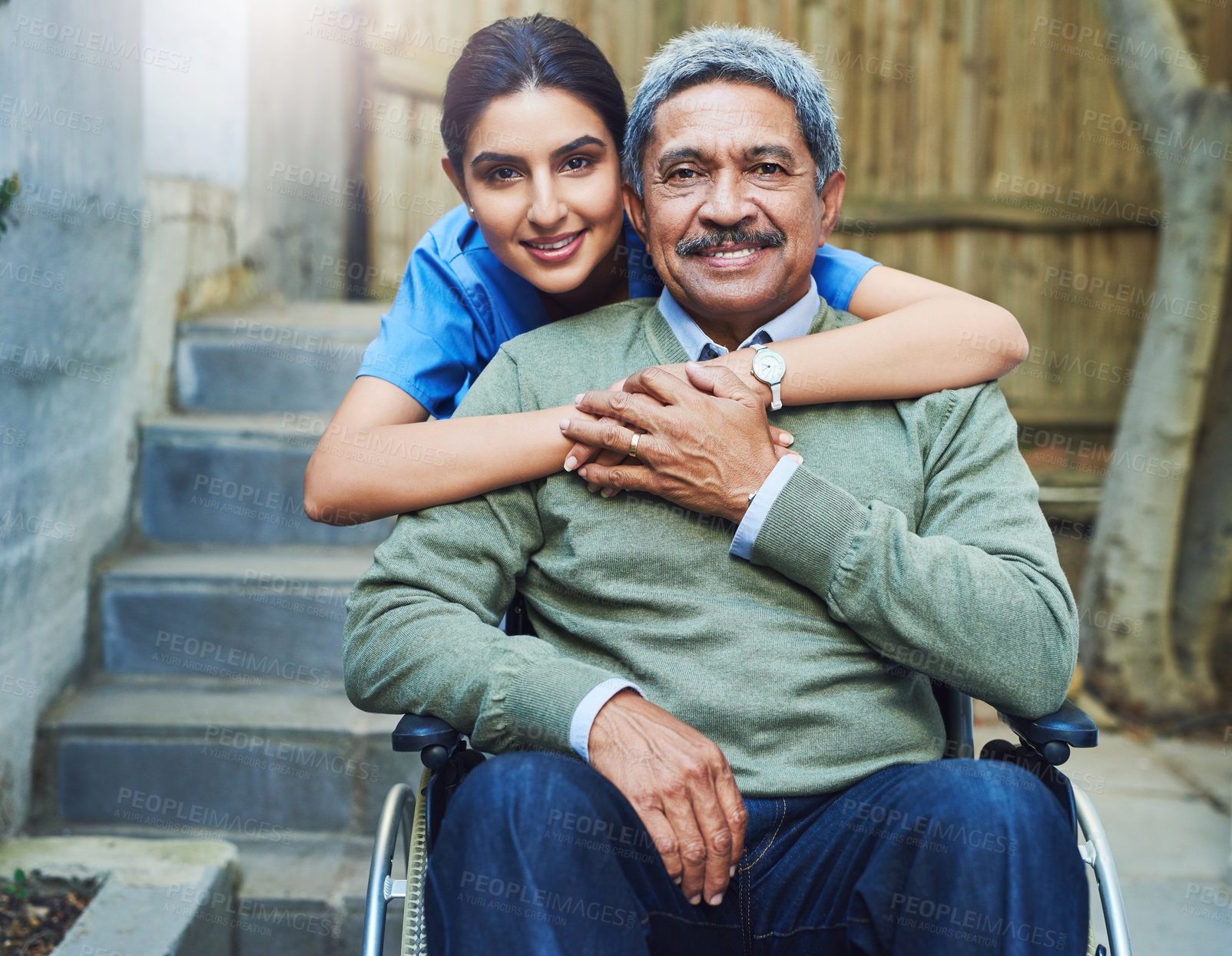 Buy stock photo Portrait of a cheerful young female nurse holding a elderly patient in a wheelchair as support outside during the day