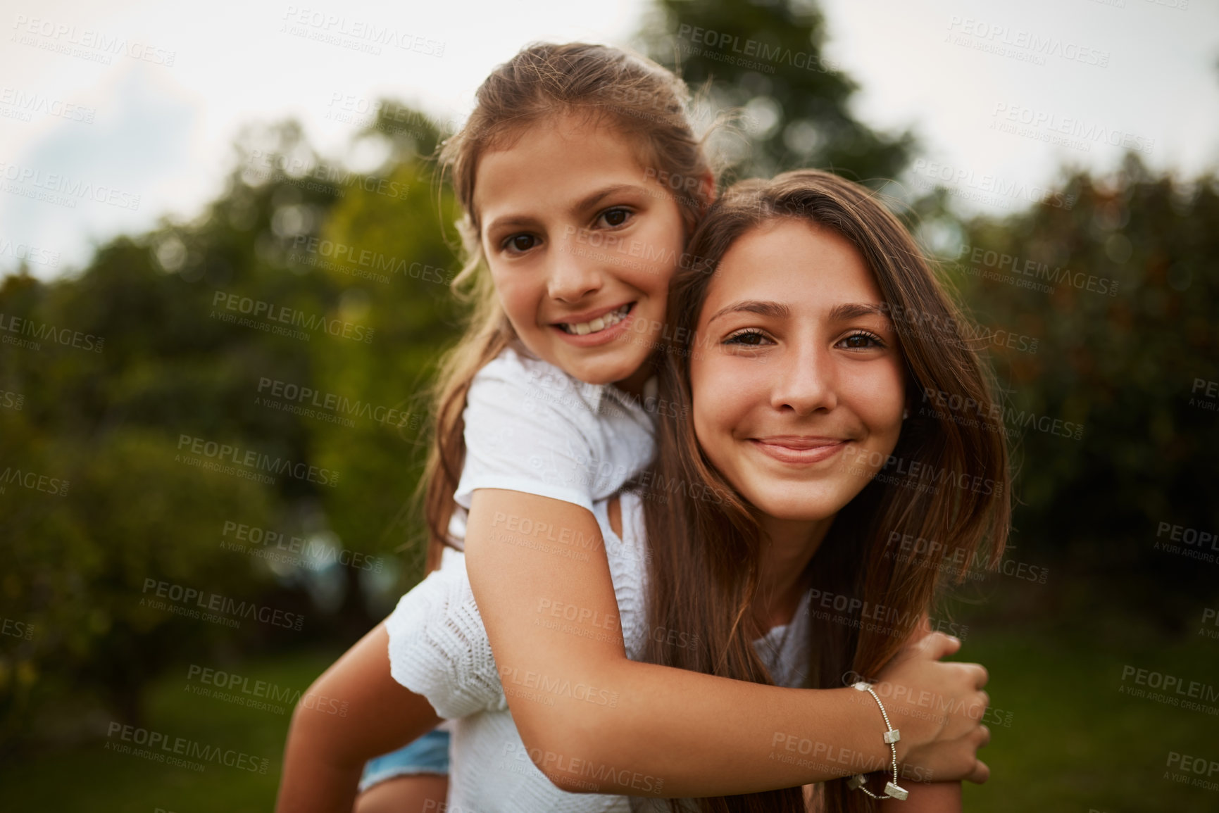 Buy stock photo Cropped portrait of a young girl giving her younger sister a piggyback ride outdoors