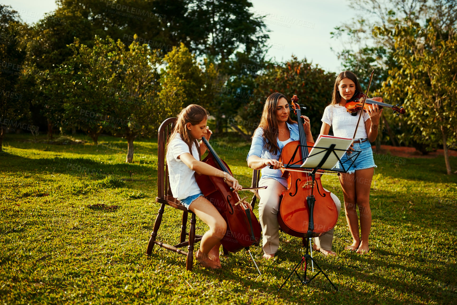 Buy stock photo Shot of a beautiful mother playing instruments with her adorable daughters outdoors