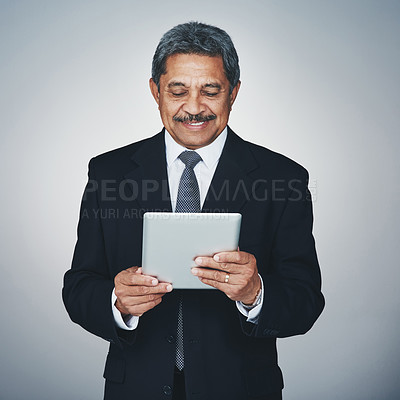 Buy stock photo Studio shot of a mature businessman using a digital tablet against a grey background