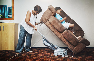Buy stock photo Shot of a grandmother vacuuming under a couch which her grandson is lying on at home