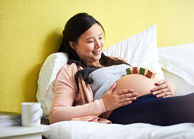 Buy stock photo Shot of a pregnant woman lying down with wooden baby blocks on her belly at home