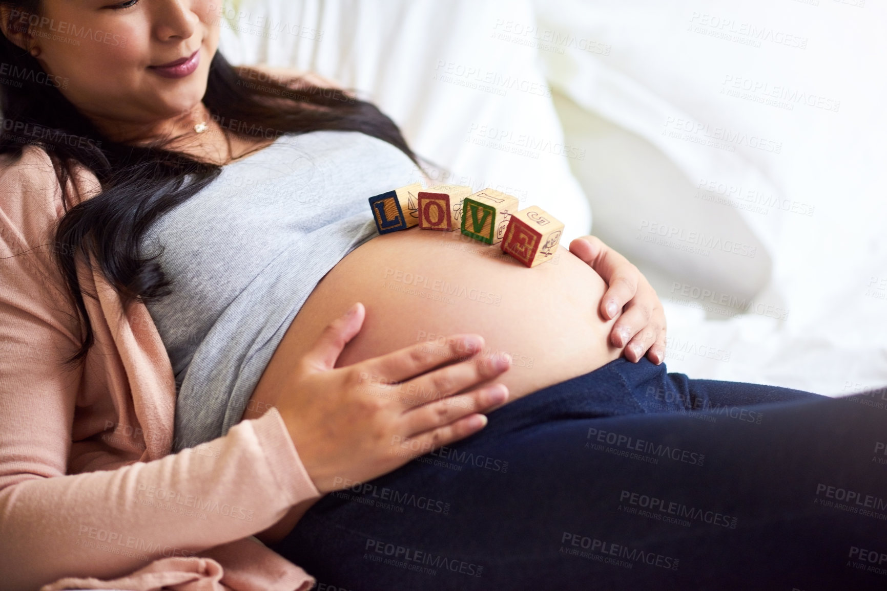 Buy stock photo Shot of a pregnant woman lying down with wooden baby blocks on her belly at home