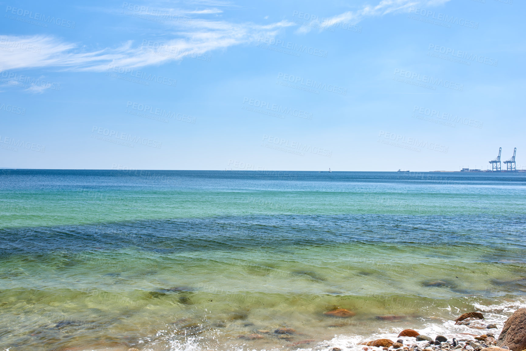 Buy stock photo Landscape view of a blue ocean with clear skies on the horizon on a warm summer day. Little waves crash on a quiet calm rocky shore in the mediterranean sea. Panoramic coastline location for tourist