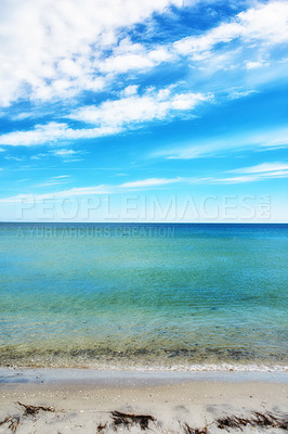 Buy stock photo Copy space at the beach with a cloudy blue sky background above the horizon. Calm ocean waters washing onto a sea shore. Peaceful scenic coastal landscape for a relaxing and zen summer getaway