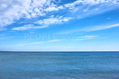Buy stock photo Copy space at sea with a cloudy blue sky background. Calm ocean water across an empty beach with a sailboat cruising in the horizon. Scenic and tranquil landscape view for a peaceful summer holiday