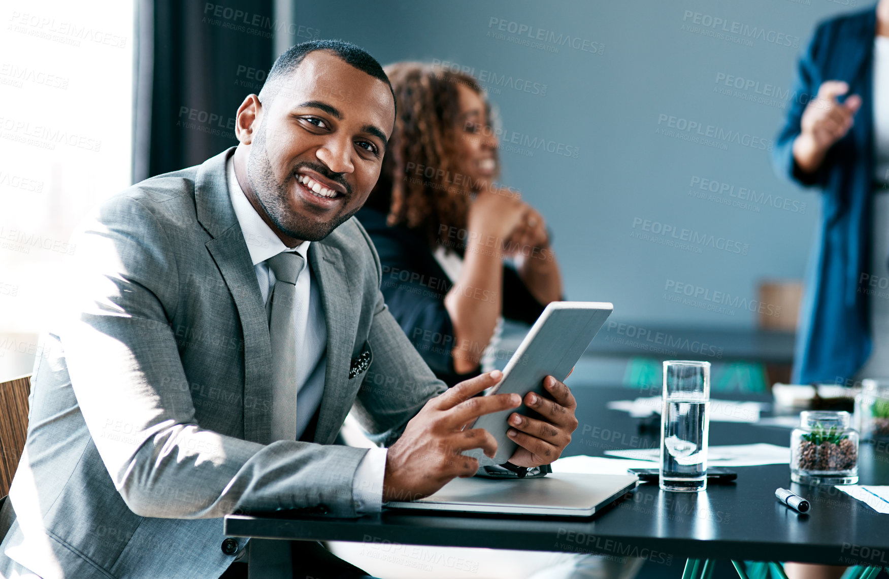 Buy stock photo Cropped portrait of a handsome young businessman working on his tablet during a meeting in the boardroom