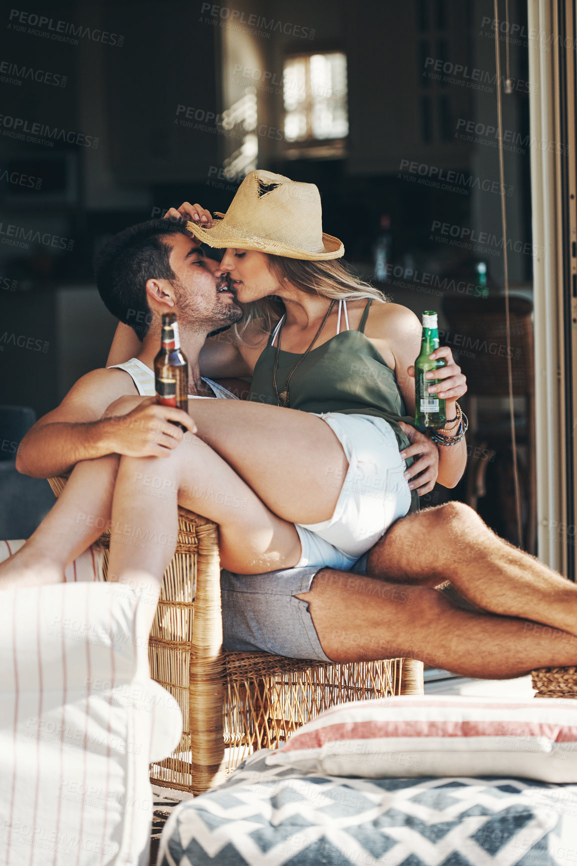 Buy stock photo Cropped shot of an affectionate young couple kissing while enjoying some beers on their patio
