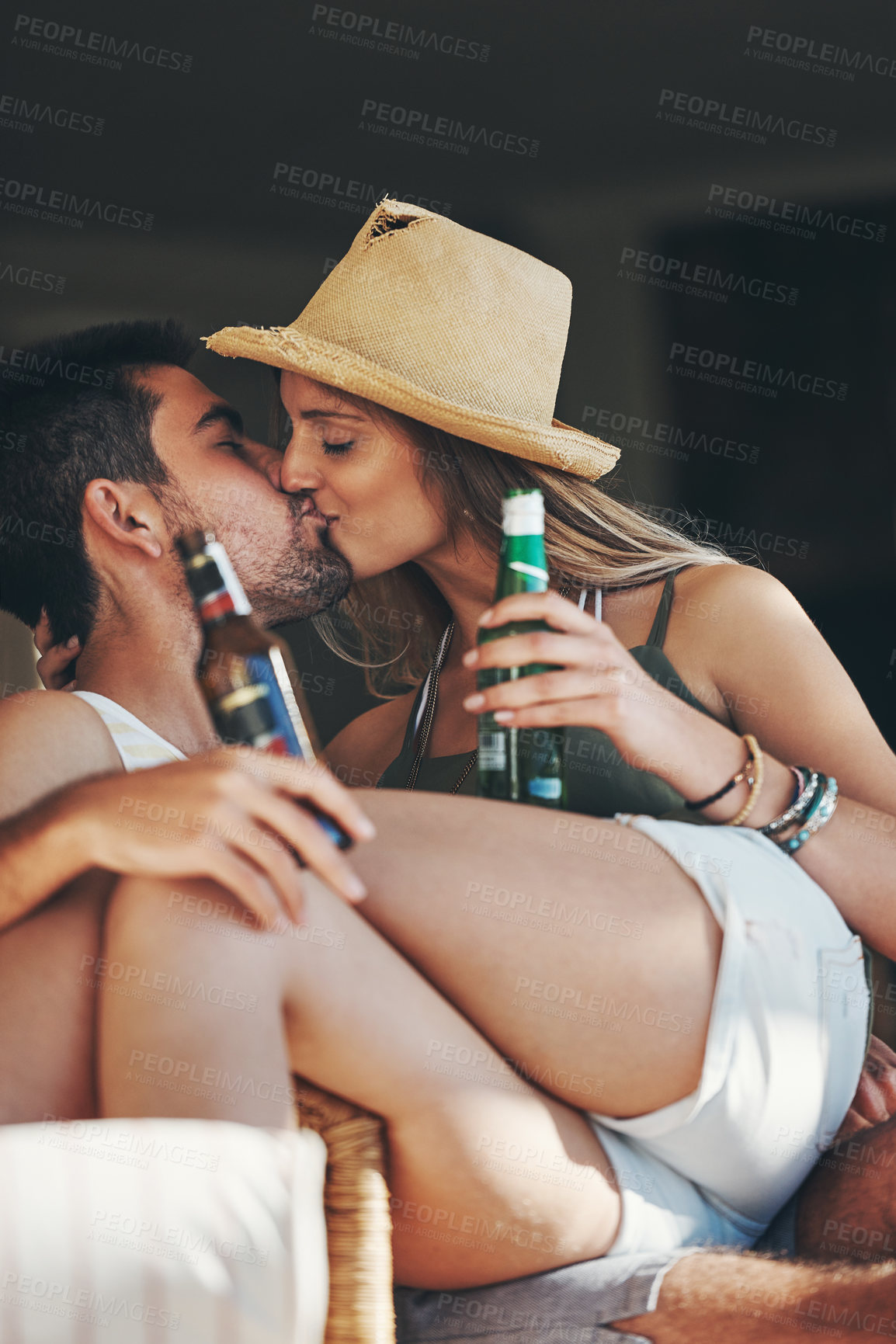 Buy stock photo Cropped shot of an affectionate young couple kissing while enjoying some beers on their patio