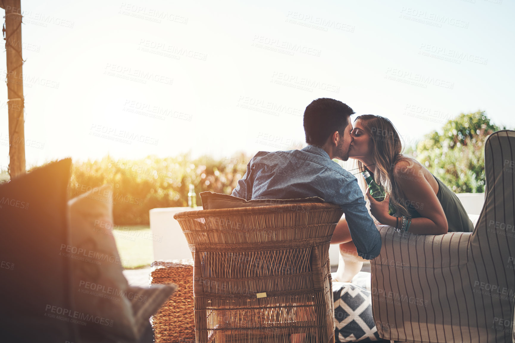 Buy stock photo Rearview shot of an affectionate young couple kissing while enjoying some beers on their patio