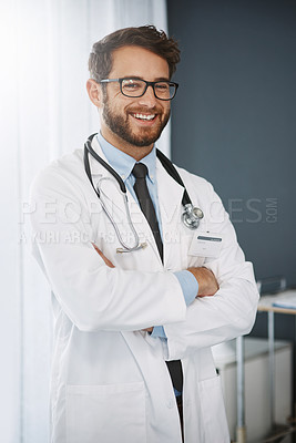 Buy stock photo Cropped portrait of a confident young male doctor standing with his arms folded inside of a hospital