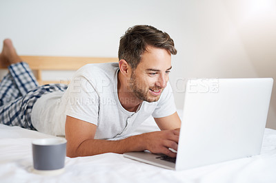Buy stock photo Shot of a young man using a laptop while having coffee on his bed at home