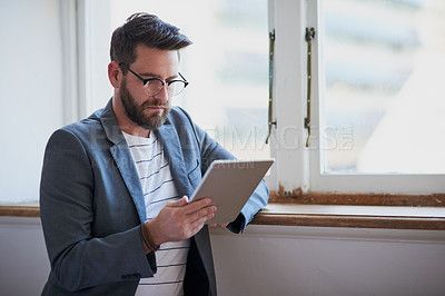 Buy stock photo Cropped shot of a handsome young businessman working on a tablet while standing by his bedroom window